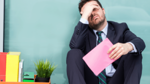 Frustrated man in a business suit sitting on the ground with his belongings in a box after losing his job