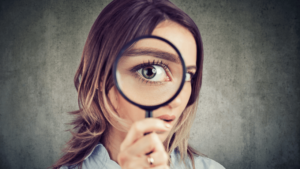 Woman holding a magnifying glass in front of her eye, enlarging it comically.